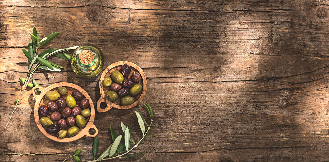 A vintage-looking table with olives, olive oil, and olive leaves